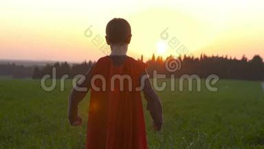 日落时穿着超级英雄斗篷的男孩站在田野里
